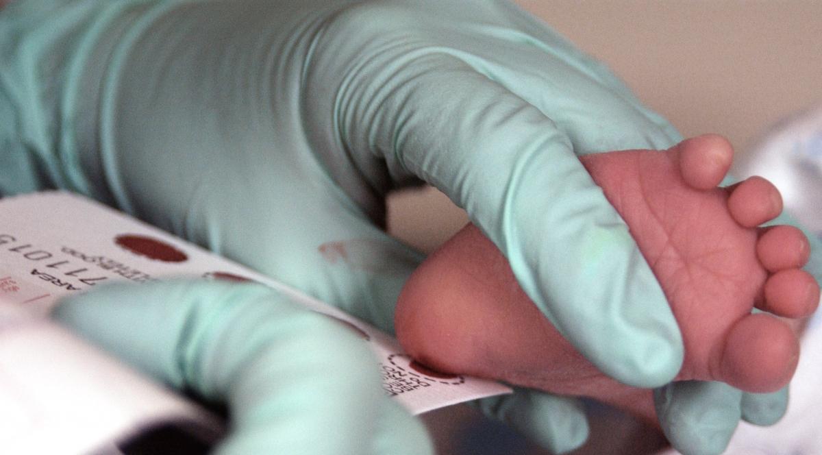 A doctor conducts a heel stick test on a newborn.